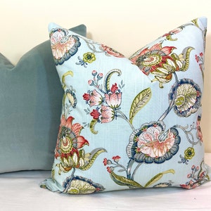 May include: A light blue throw pillow with a floral pattern featuring red, pink, green, and blue flowers. The pillow is made of a soft, textured fabric.