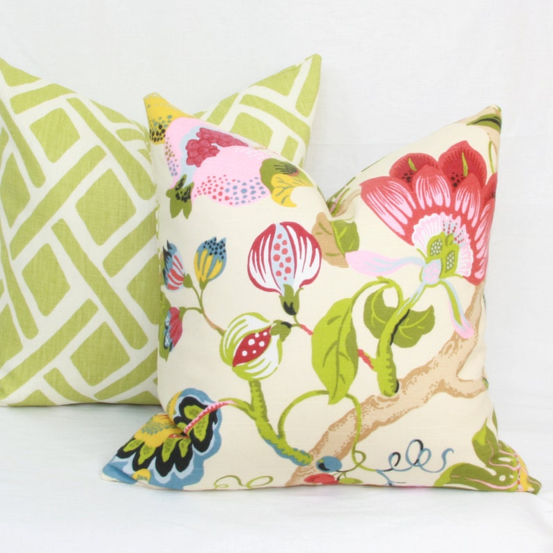 May include: Two decorative throw pillows, one with a green and white geometric pattern and the other with a floral pattern featuring pink, red, yellow, and green flowers on a cream background.