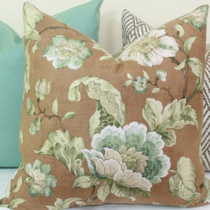 May include: A brown throw pillow with a floral pattern featuring green and white flowers. The pillow is surrounded by other pillows in green and brown.