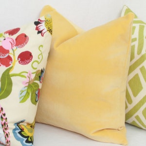 May include: Three decorative throw pillows. One pillow has a floral pattern with red, pink, and green accents. Another pillow is a solid yellow. The third pillow has a geometric pattern with green and white accents.