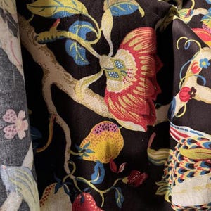 May include: Black fabric with a floral pattern featuring red, yellow, and white flowers, green leaves, and a white bird. The fabric has a textured surface.