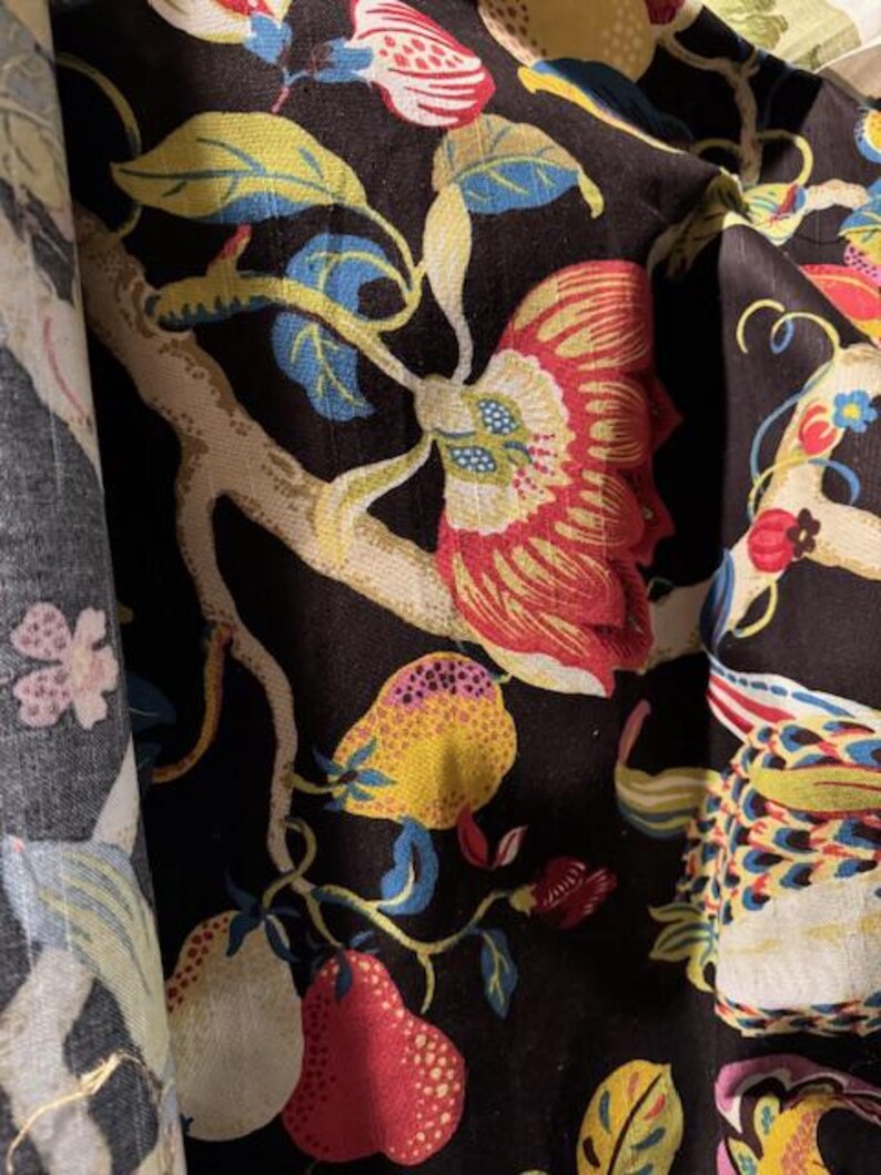 May include: Black fabric with a floral pattern featuring red, yellow, and white flowers, green leaves, and a white bird. The fabric has a textured surface.