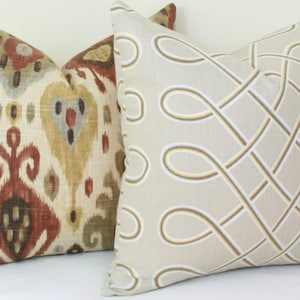 May include: Two decorative throw pillows. One pillow has a brown, red, and beige ikat pattern. The other pillow is beige with a white and yellow geometric pattern.