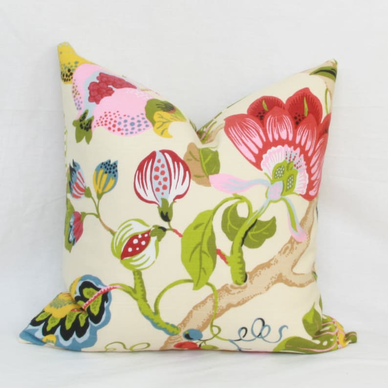 May include: A cream-colored pillow with a floral pattern. The flowers are pink, red, yellow, and green. The pillow is made of fabric and has a square shape.