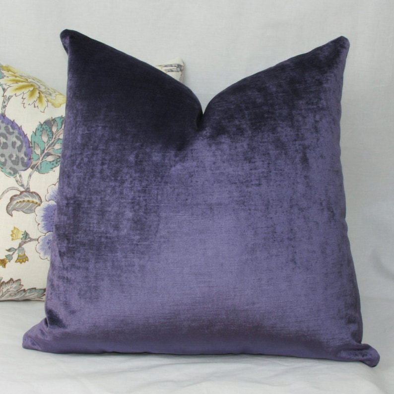 May include: A deep purple velvet cushion with a soft, textured surface. The cushion is square and has a simple design.