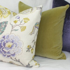 May include: Three decorative throw pillows, one with a floral pattern in shades of purple, yellow, and green on a white background, one in a solid olive green, and one in a solid purple.