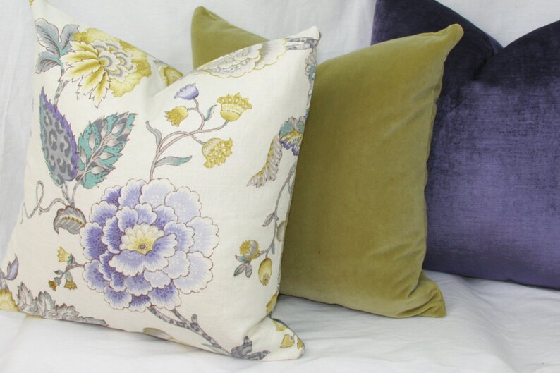 May include: Three decorative throw pillows, one with a floral pattern in shades of purple, yellow, and green on a white background, one in a solid olive green, and one in a solid purple.