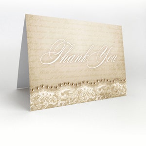 May include: A beige thank you card with a white lace border and pearl accents. The card has a vintage, handwritten look and says "Thank You" in a cursive font.