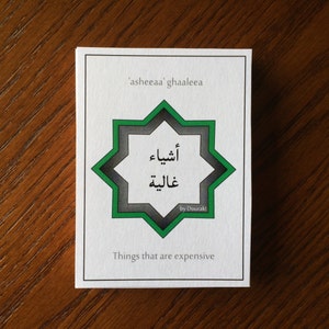 Peut inclure: Une carte blanche avec un motif d'étoile vert et gris. La carte contient du texte arabe qui se lit "'ashee'aa' ghaalee'a" et "أشياء غالية" qui se traduit par "Choses qui sont chères". La carte contient également le texte "by Duarak!" en bas.