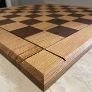 May include: A wooden chessboard with a light brown and dark brown checkered pattern. The board is made of oak wood and has a beveled edge.