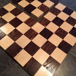 May include: A wooden chessboard with alternating light and dark squares. The squares are made of maple and dark wood. The board is in two pieces.