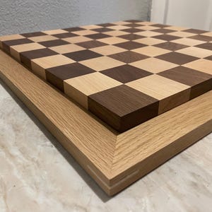 May include: A wooden chessboard with a light wood and dark wood checkerboard pattern. The board is framed in a light wood frame.