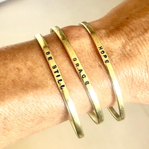 May include: Three gold-toned bracelets with the words "Hope", "Grace", and "Be Still" engraved on them.