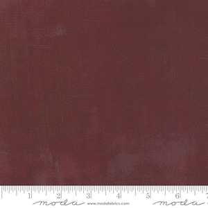 May include: A close-up of a deep red fabric with a subtle textured pattern. The fabric is measured with a ruler that reads "moda" and includes the website address "www.modafabrics.com".