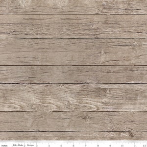 May include: A close-up of a weathered woodgrain background with a ruler showing inches. The wood is a light brown color with a natural grain pattern.