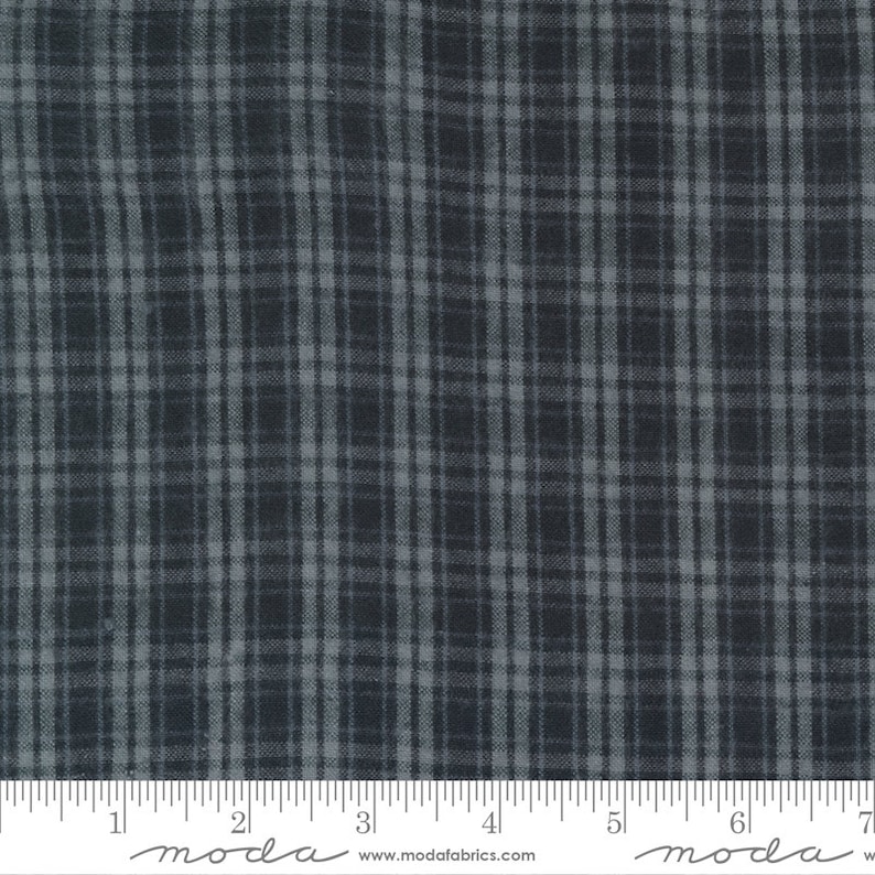 May include: A close-up of a dark gray and light gray plaid fabric. The fabric has a subtle texture and a slightly faded look. The fabric is measured in inches on a ruler.