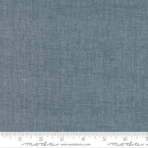 May include: A close-up of a blue fabric with a textured woven pattern. The fabric is measured with a ruler in inches. The ruler has the word "moda" printed on it.