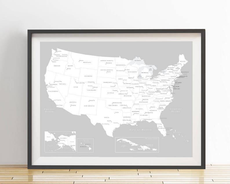 May include: Framed grayscale map of the United States, including Alaska, Hawaii, and the Caribbean. The map is in a black frame and is displayed on a white wall. The map shows state names and major bodies of water.