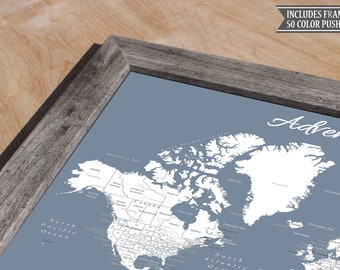 May include: A framed world map with a blue background and white countries. The map is titled "Adventure" and includes 50 color push pins. The frame is made of gray wood.