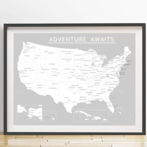 May include: Framed map of the United States in grayscale, with state names and major cities labeled. The phrase "ADVENTURE AWAITS" is printed at the top. The map is set against a light gray background, framed in black.