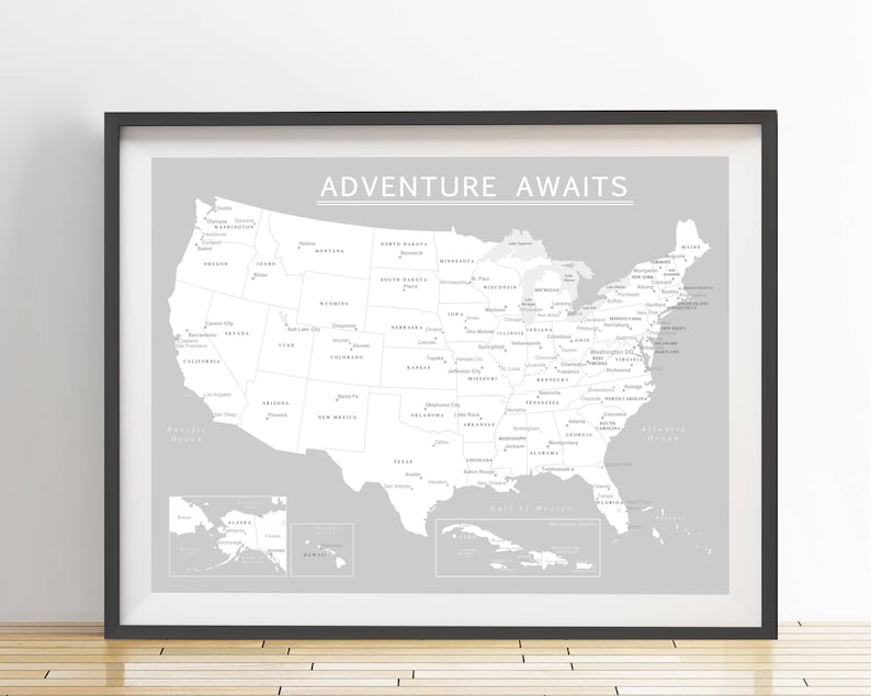 May include: Framed map of the United States in grayscale, with state names and major cities labeled. The phrase "ADVENTURE AWAITS" is printed at the top. The map is set against a light gray background, framed in black.