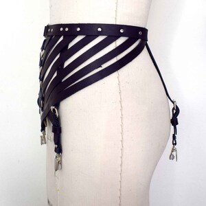 K&ouml;nnte beinhalten: Ein schwarzes Ledergeschirr mit geometrischem Design und silbernen Metalldetails. Das Geschirr hat verstellbare Riemen und Schnallen.
