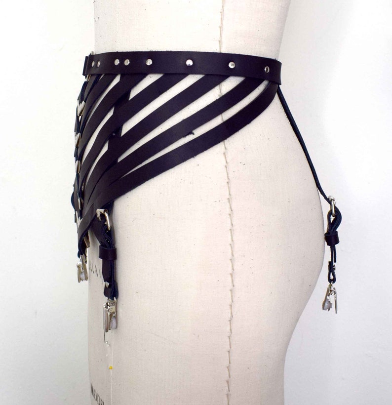 K&ouml;nnte beinhalten: Ein schwarzes Ledergeschirr mit geometrischem Design und silbernen Metalldetails. Das Geschirr hat verstellbare Riemen und Schnallen.