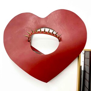 May include: A red leather heart-shaped collar with gold-coloured spikes around the opening.