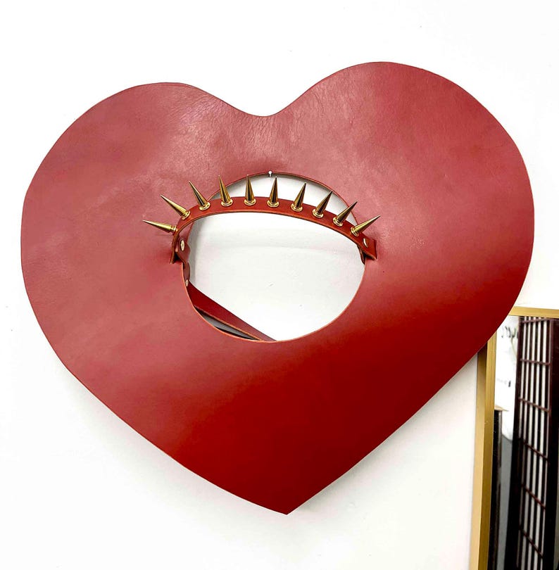 May include: A red leather heart-shaped collar with gold-coloured spikes around the opening.
