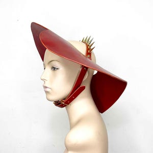 May include: A red leather hat with a wide brim and a spiked band. The hat is worn on a mannequin's head.