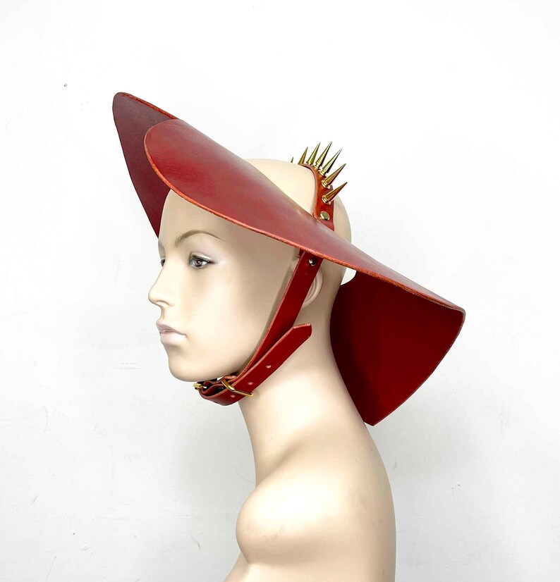 May include: A red leather hat with a wide brim and a spiked band. The hat is worn on a mannequin's head.