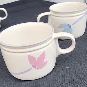 Peut inclure: Deux tasses en céramique blanche avec des motifs floraux. Une tasse a un motif de fleur rose et l'autre a un motif de fleur bleue.