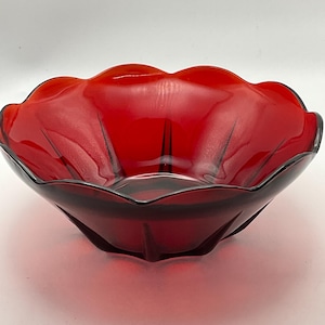 May include: A vibrant red glass bowl with a scalloped rim. The bowl has a deep, rounded shape and a glossy finish. The interior features subtle black lines radiating from the center, adding a touch of detail to the design.