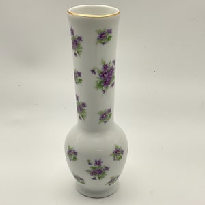 May include: White porcelain vase with a gold rim and a bulbous base. The vase is adorned with clusters of purple violets and green leaves. A decorative floral vase for home decor.