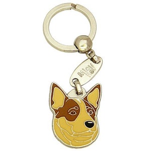 May include: A metal keychain featuring a dog's head with brown and yellow enamel. The keychain has a silver ring and a small tag with the text "MiaV". The dog's head is detailed with black eyes and nose.