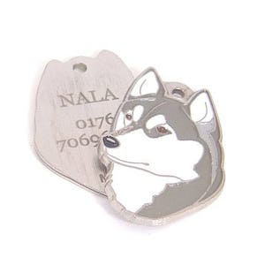 May include: A silver pet tag with a husky design. The tag features the name "NALA" and a phone number. The husky design is gray, white, and black with brown eyes. The tag has a small hole for attachment.