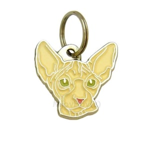 May include: A gold-toned metal cat charm with a light yellow enamel finish depicting a Sphynx cat with green eyes. The charm has a ring attached for attaching to a collar or keychain.