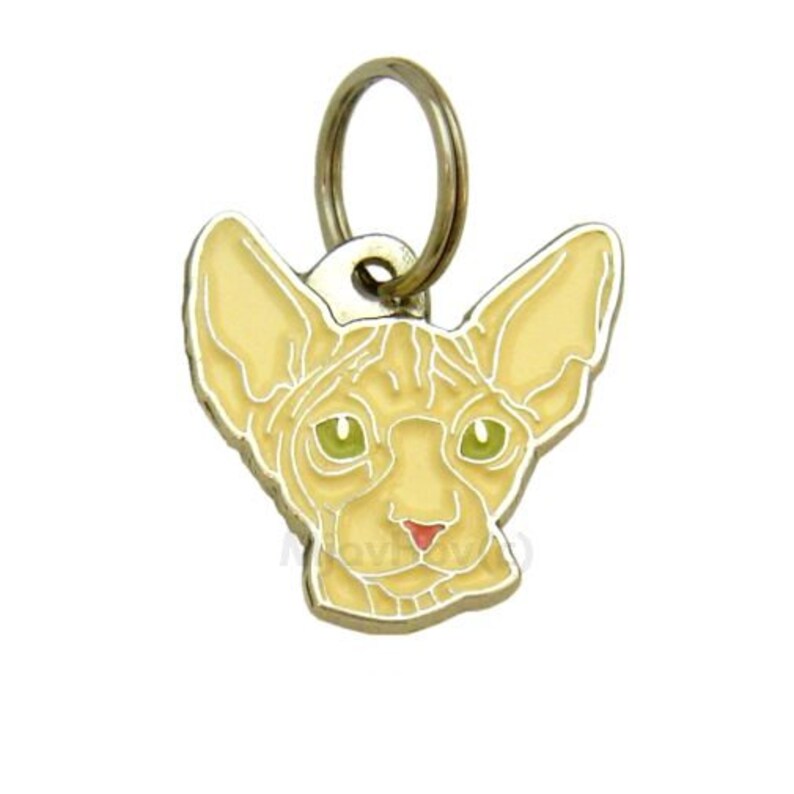 May include: A gold-toned metal cat charm with a light yellow enamel finish depicting a Sphynx cat with green eyes. The charm has a ring attached for attaching to a collar or keychain.
