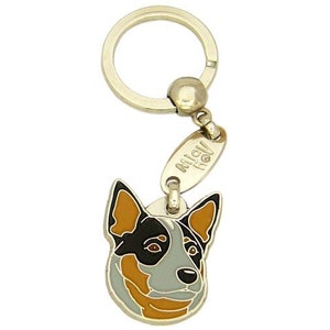 May include: A gold-colored metal keychain featuring a dog's head pendant. The pendant is a detailed, colorful illustration of a dog's face with black, tan, and gray markings. The keychain includes a split ring and a small tag with text.