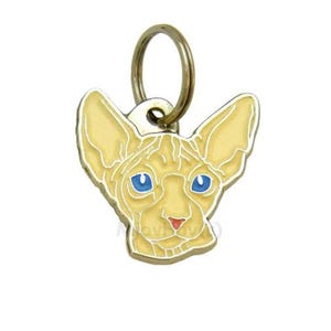 May include: A gold-colored metal cat charm with a light yellow Sphynx cat head design. The cat has blue eyes and a pink nose.