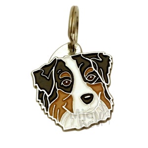 Puede incluir: Una chapa metálica para mascotas con forma de cabeza de pastor australiano. La chapa presenta un diseño detallado con colores negro, marrón, blanco y beige, y un anillo plateado para sujetar.