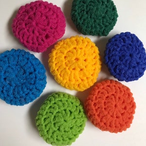 May include: Seven crocheted dishcloths in various colours, including green, blue, yellow, orange, and pink. The dishcloths are round and have a textured surface.