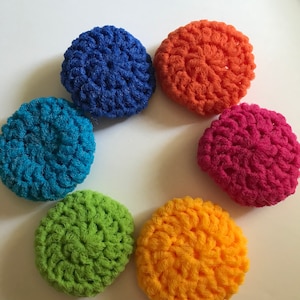 May include: Six colorful crocheted scrubbers in a rainbow pattern. The scrubbers are blue, teal, green, yellow, orange, and pink.