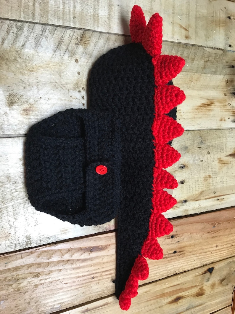 May include: Black crocheted baby dinosaur costume with red spikes and a button fastening.