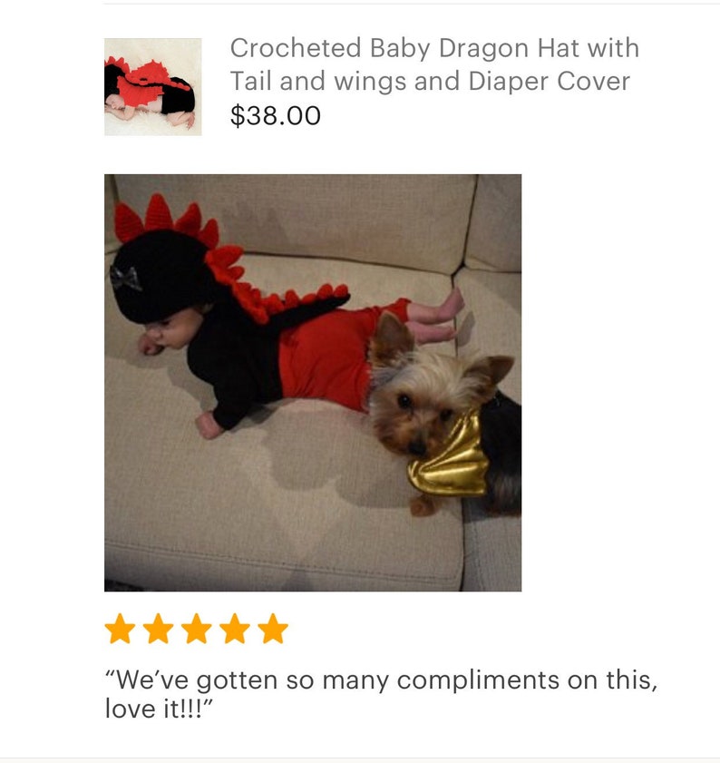 May include: A baby wearing a crocheted red and black dragon costume with a tail and wings. The baby is lying on a sofa with a small dog wearing a gold wing costume.