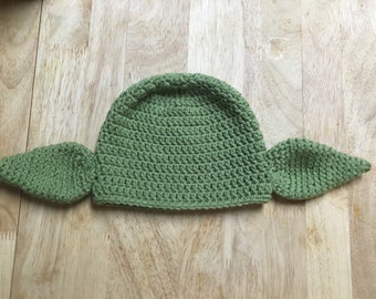 May include: Green crocheted hat with two ear-like flaps, resembling a popular fictional character.