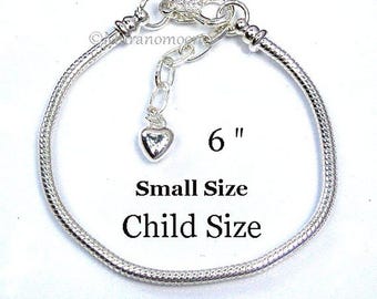 May include: A silver-tone snake chain bracelet measuring 6 inches in length. The bracelet features a lobster claw clasp, an adjustable extender chain, and a small heart-shaped charm. The text 6", Small Size, and Child Size is visible.