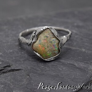May include: A silver ring with a rough, irregular shaped opal gemstone set in a textured band.