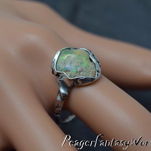 May include: A silver ring with a large, irregular shaped opal gemstone set in a textured silver band. The opal has a green, white, and brown color.