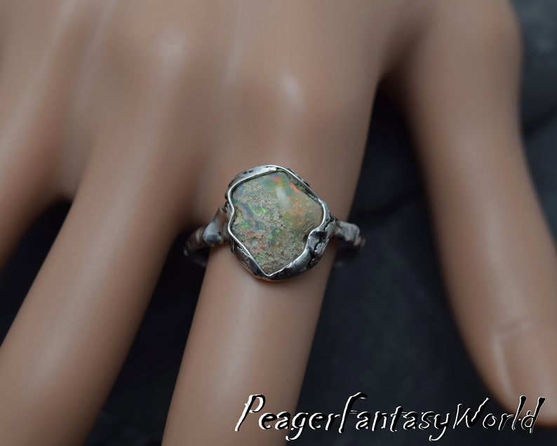 May include: A silver ring with a large, irregular shaped opal gemstone set in a textured silver band.